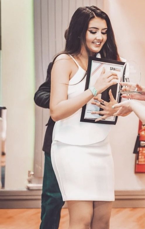 Ellie in a white dress accepting a Student Publication Association award and certificate.