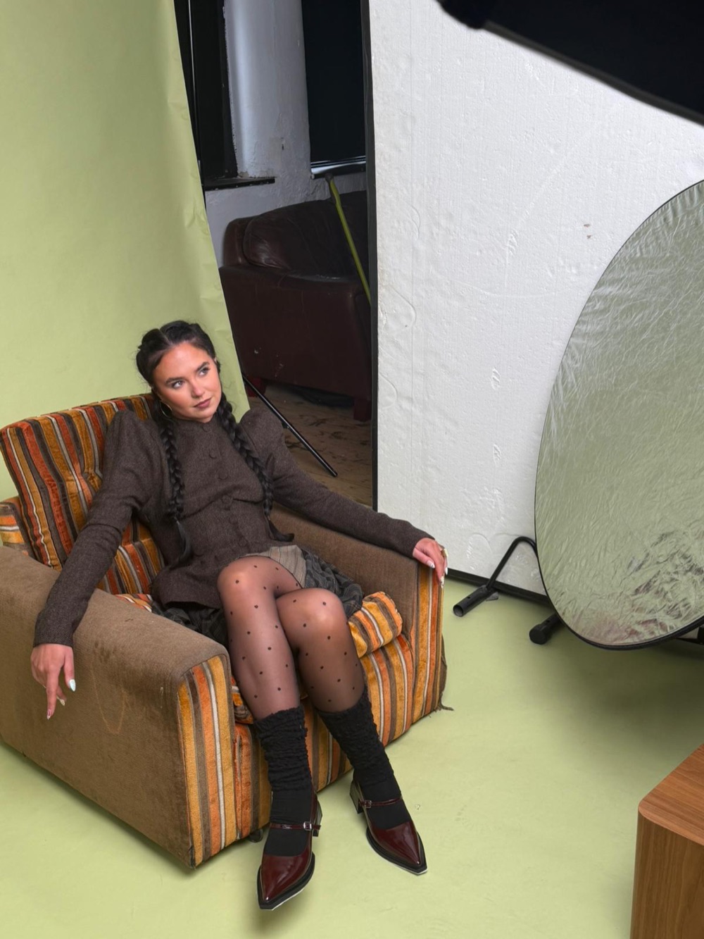 Behind the scenes: Louisa in a striped vintage armchair between takes, next to a silver light reflector.