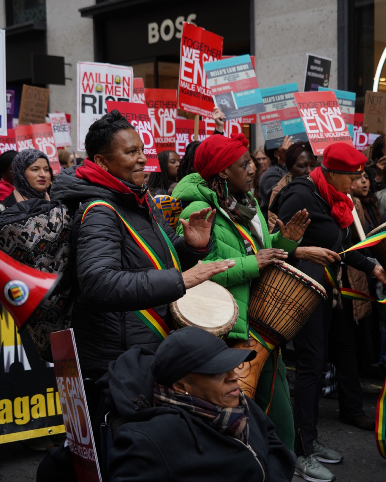 Drummers with red, gold and green sashes play djembe drums as the march passes along Regent Street.