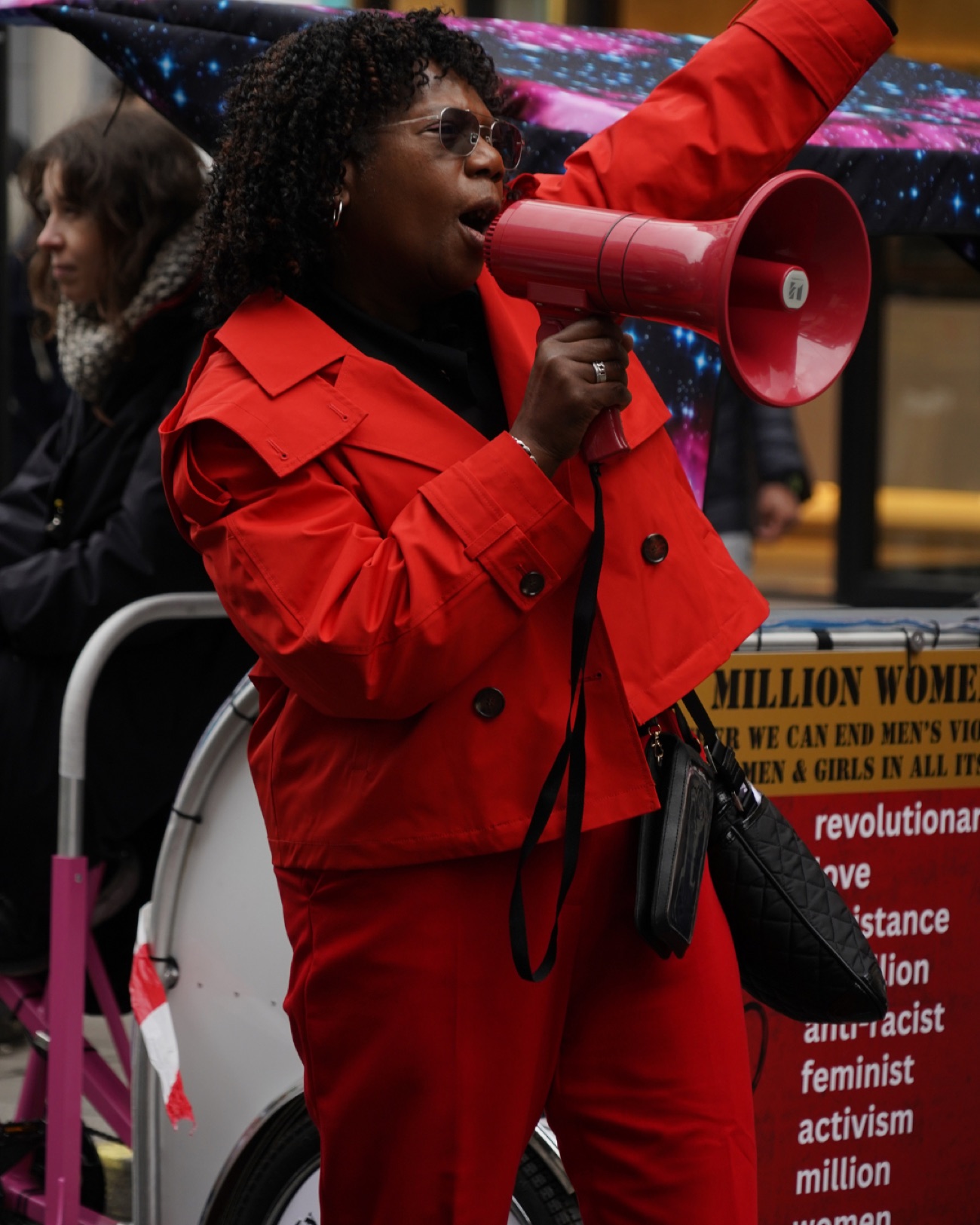A speaker in a bright red suit addresses the march through a red megaphone.