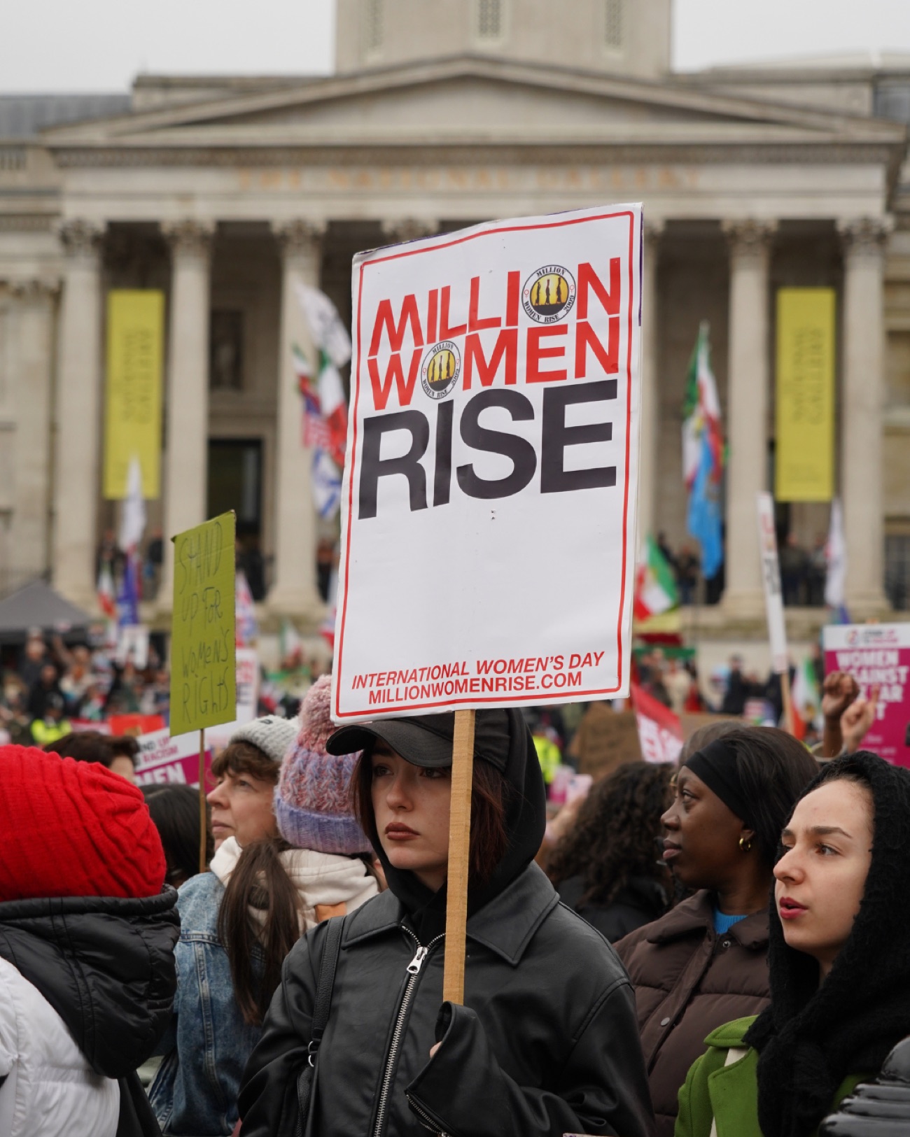A Million Women Rise placard held high in Trafalgar Square, the National Gallery behind.