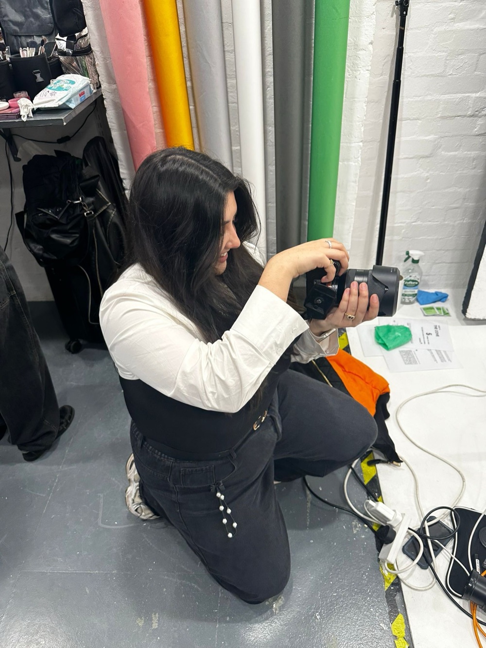 Ellie crouched in the studio directing a shoot, Sony camera in hand, colourful backdrop rolls behind her.